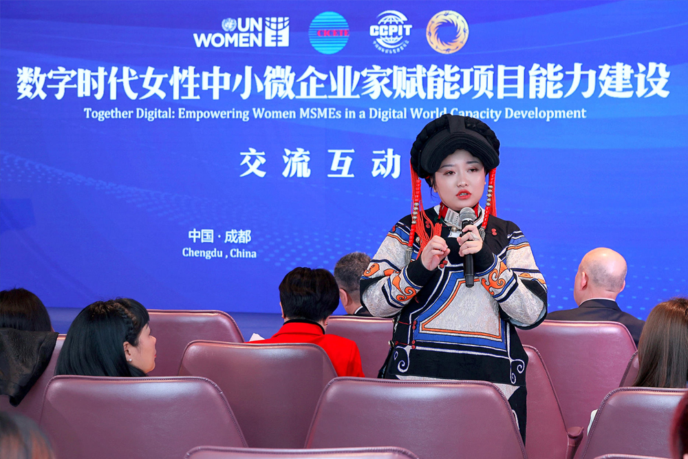 A woman standing holding a microphone and talking to an audience at an event.
